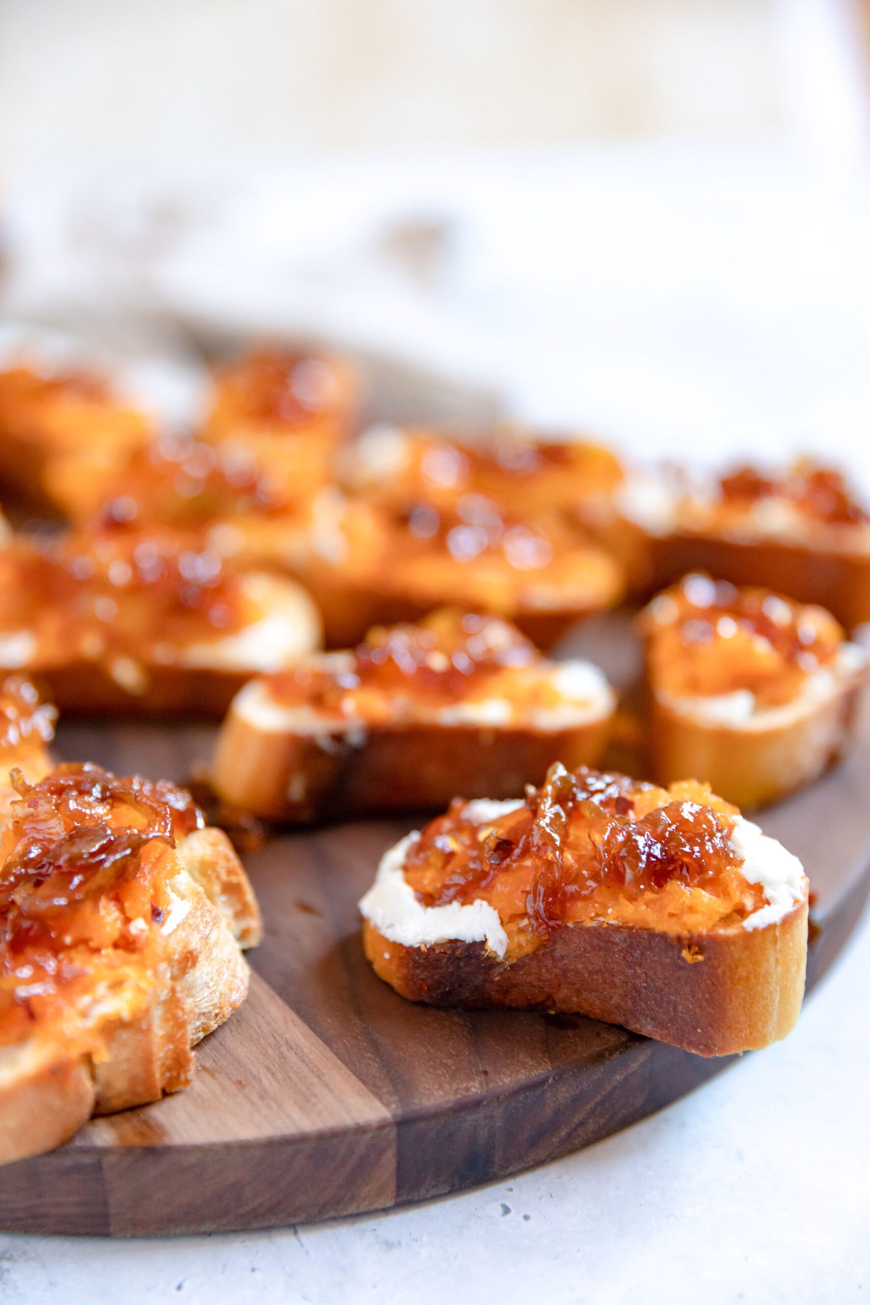 Close up of multiple toasted baguette slices each topped with spreadable ricotta cheese, mashed butternut squash, and caramelized onions placed on a dark wood cutting board.